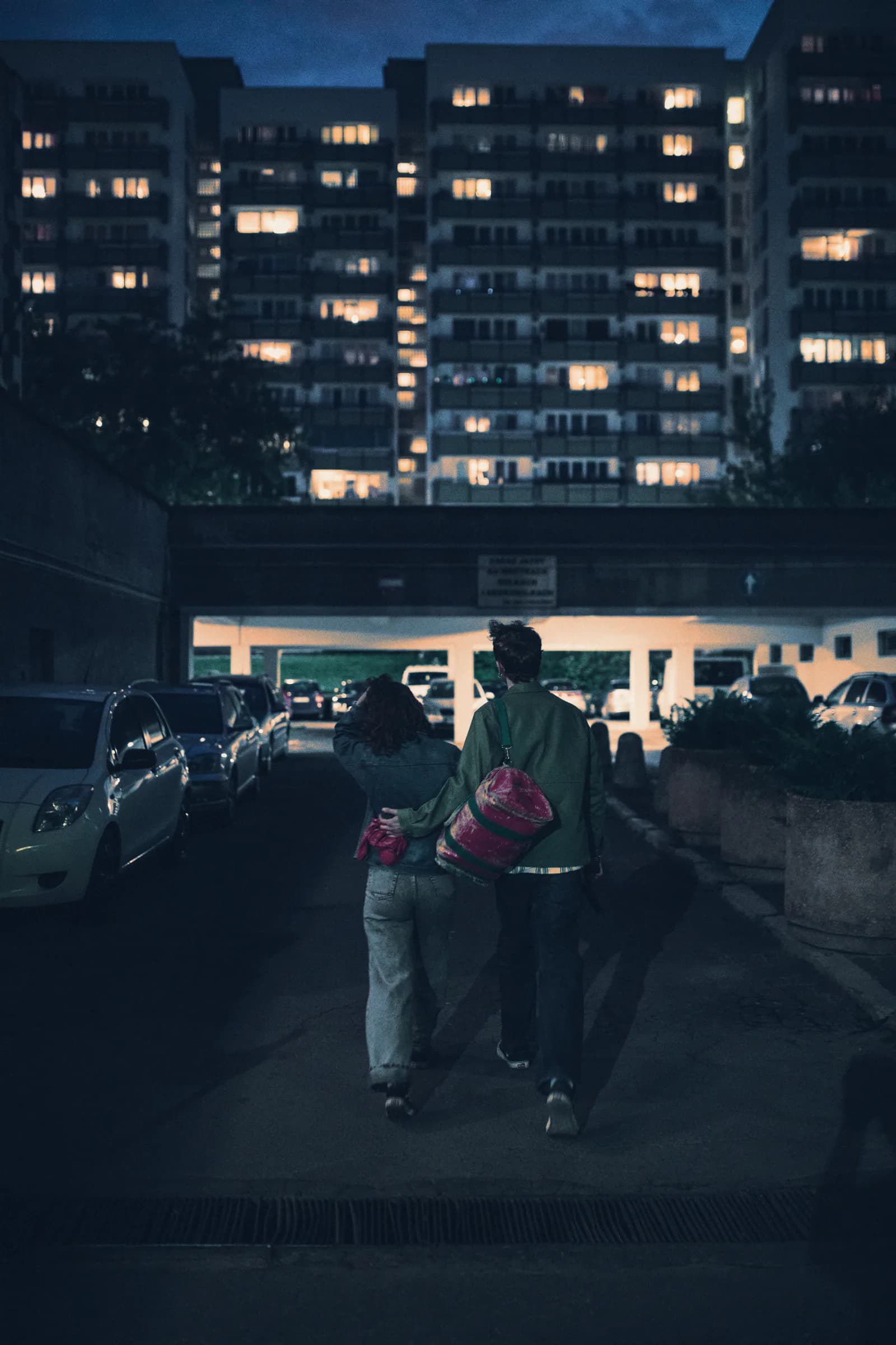 Two people walking through a car park at night, carrying bags
